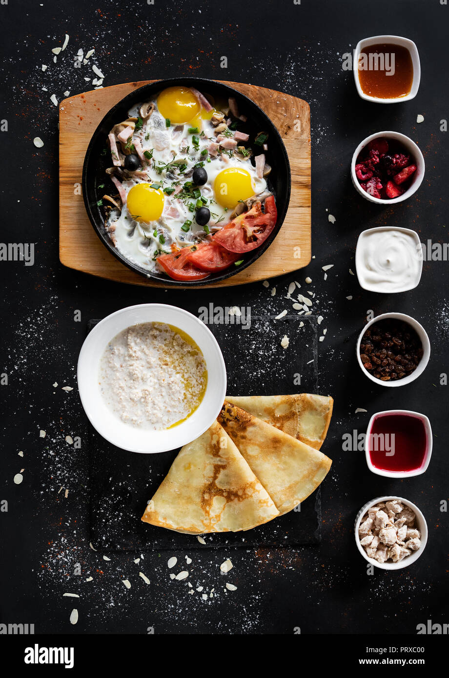 Il cibo della colazione concetto. Sfondo scuro con pan con uova con verdure, fiocchi d'avena con pancake e sei tipi di salse. Mangiare sano stile. Top v Foto Stock