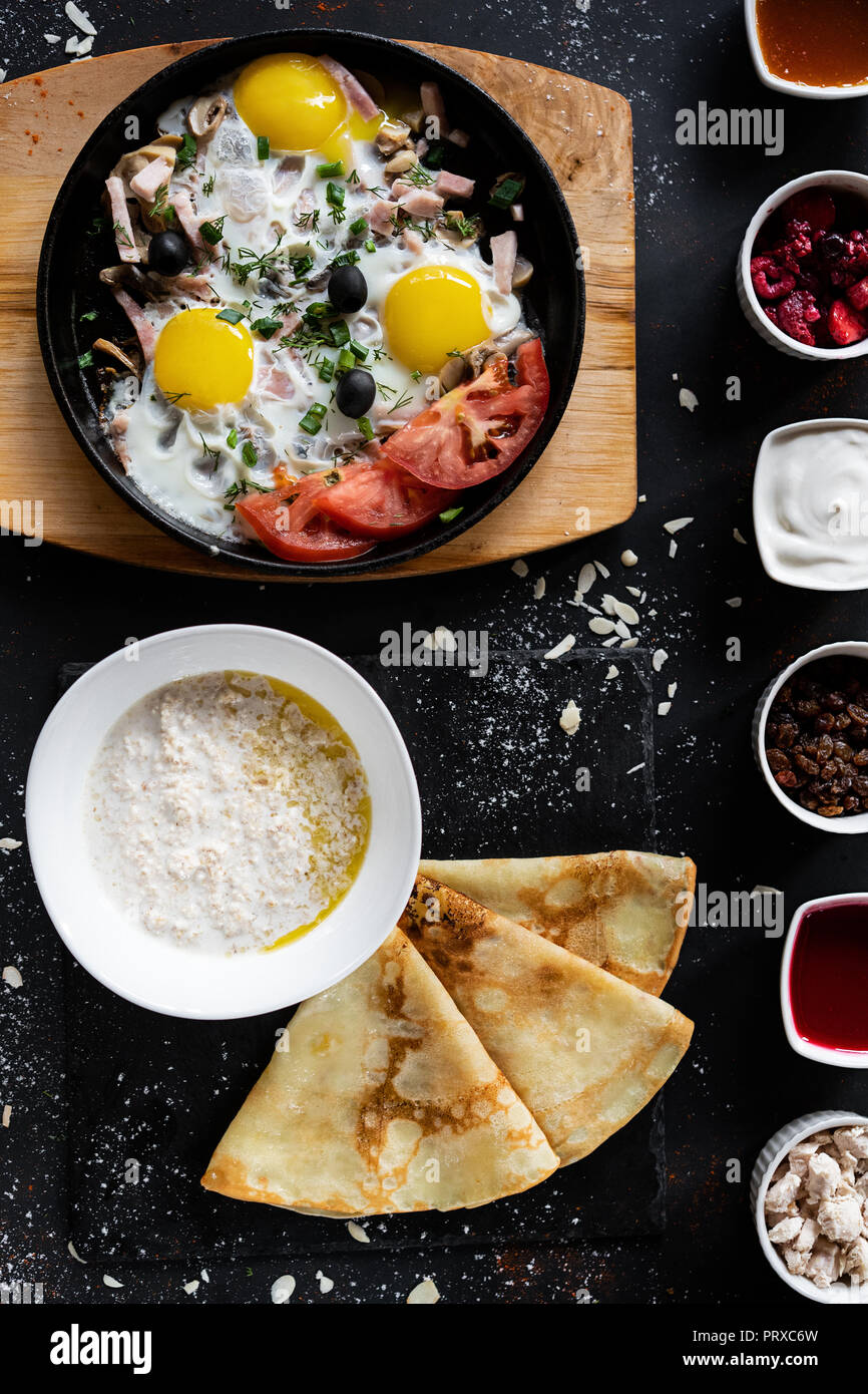 Il cibo della colazione concetto. Sfondo scuro con pan con uova con verdure, fiocchi d'avena con pancake e sei tipi di salse. Mangiare sano stile. Top v Foto Stock