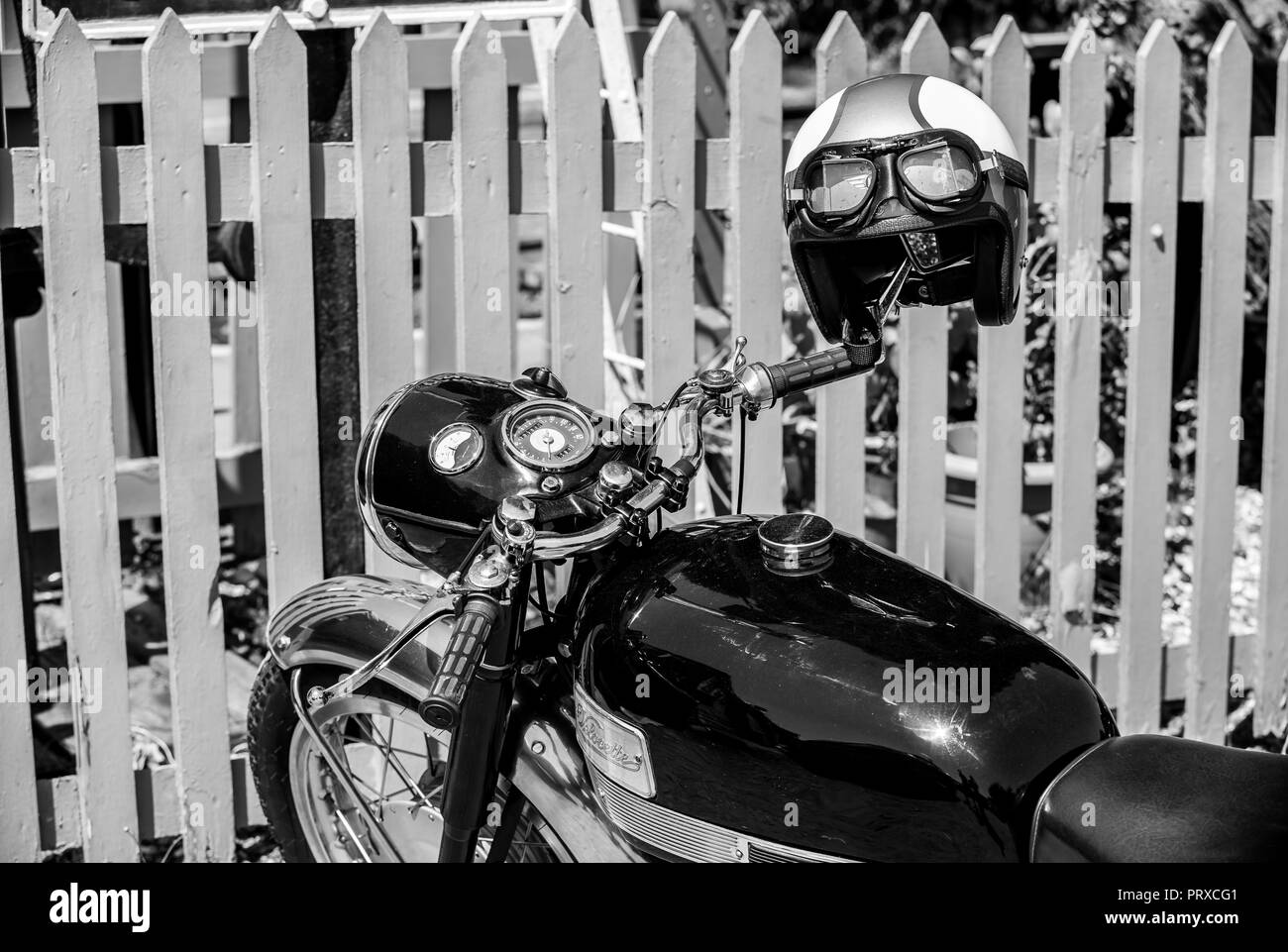 Il paesaggio in bianco e nero close up: Vellocette motocicletta vintage, casco sul manubrio, parcheggiata da Picket Fence, SVR Hampton Loade stazione, 1940's evento. Foto Stock