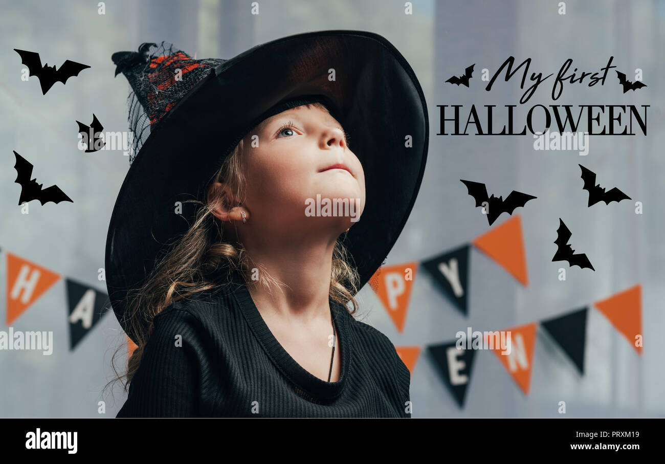 Ritratto di adorabili bambini in witch halloween costume che guarda lontano da casa con 'my prima di halloween lettering" Foto Stock