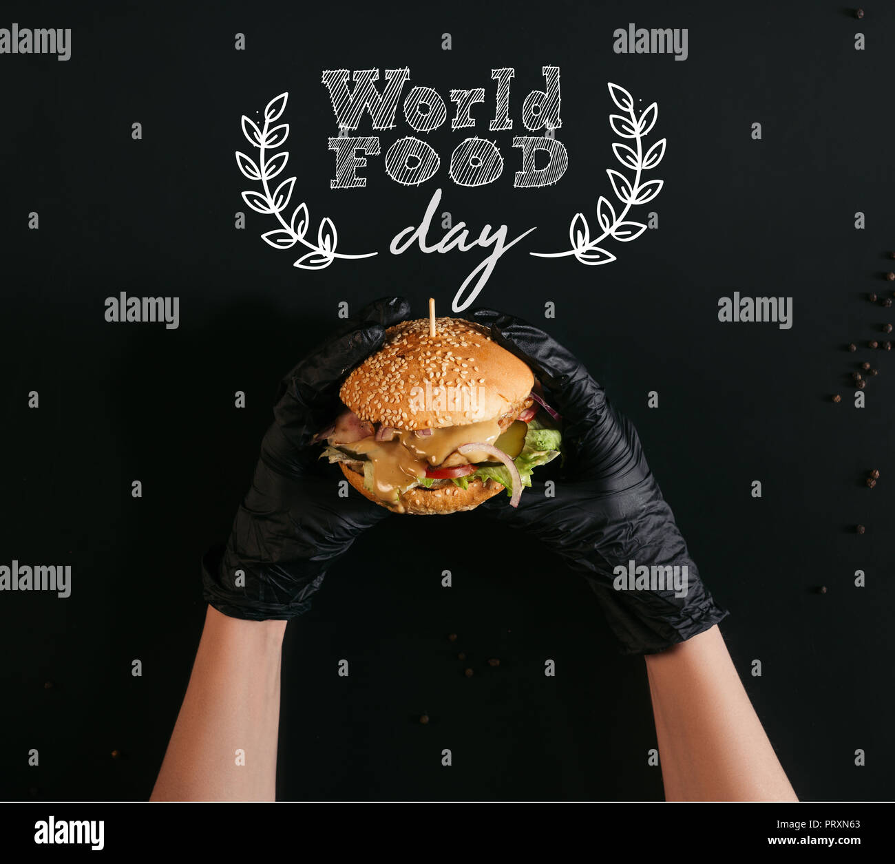 Ritagliato colpo di mani guanti in azienda deliziosi burger con la Turchia, verdure e Cesare medicazione in nero con 'world food day" scritte Foto Stock