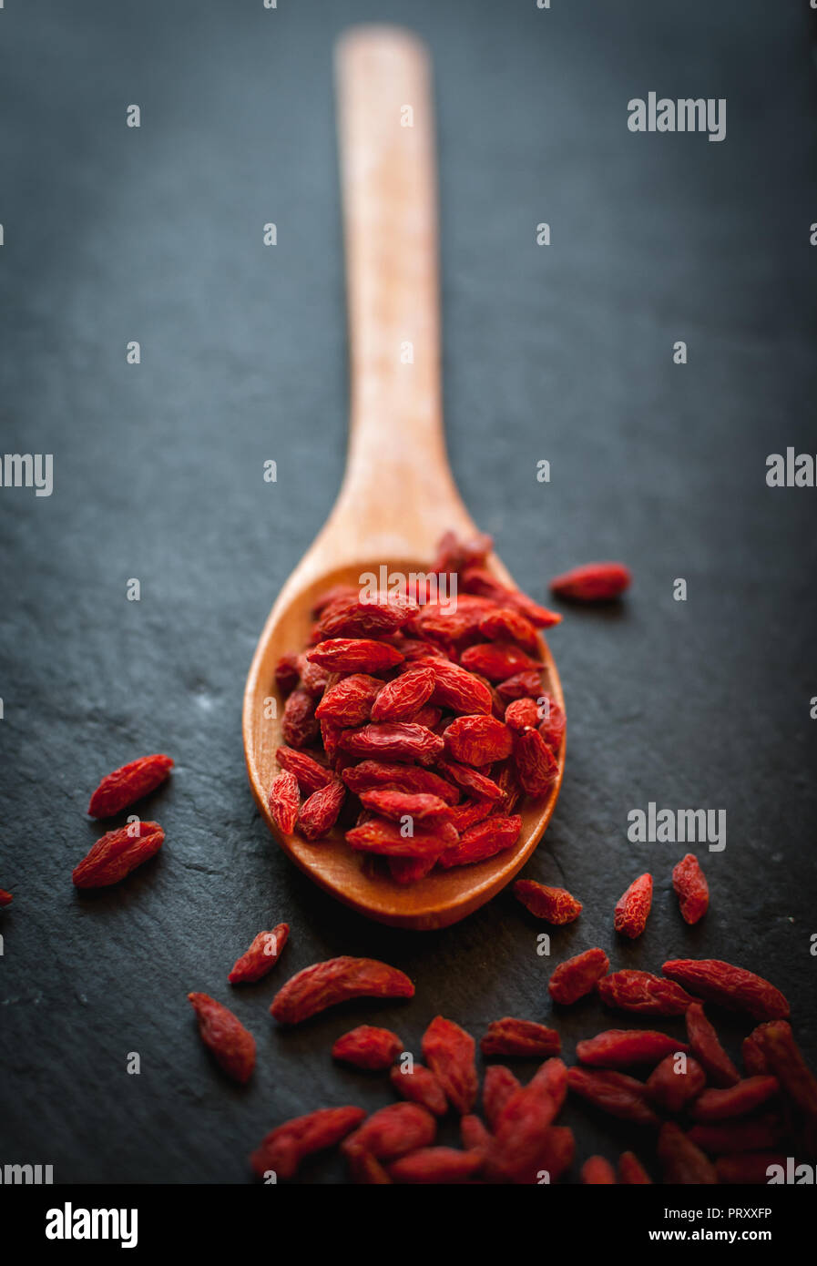 Close-up di essiccati goji bacche di cucchiaio di legno su sfondo scuro Foto Stock