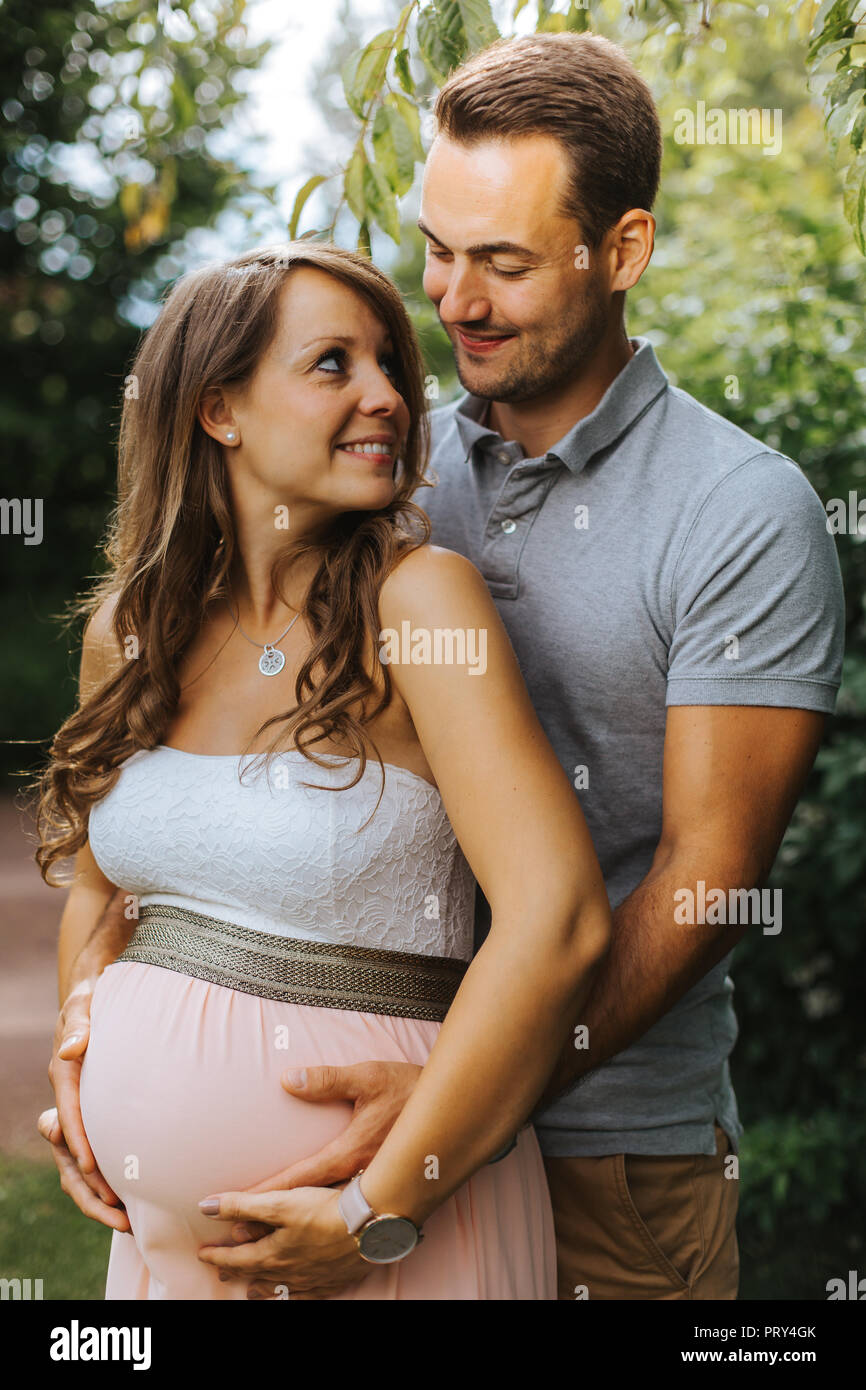 Il marito è abbracciando la sua bella moglie incinta da dietro e toccando il suo ventre Foto Stock