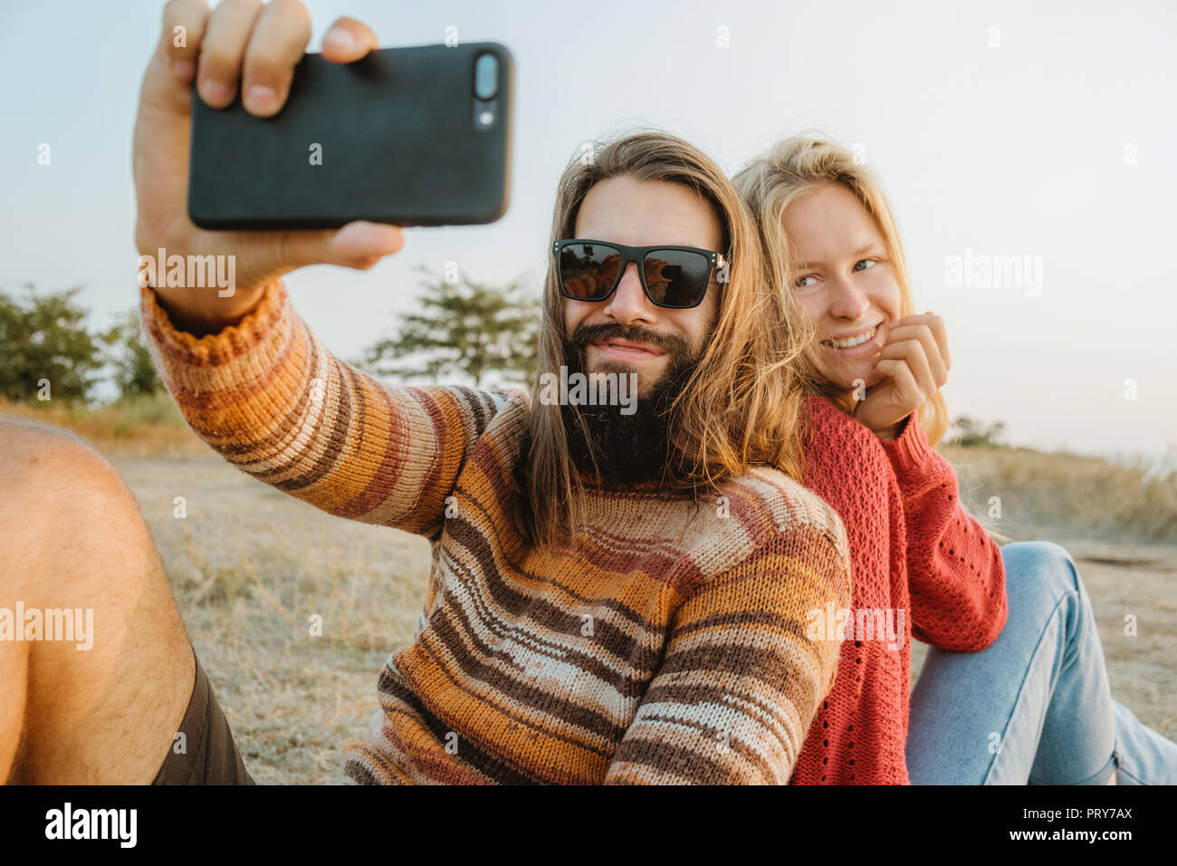 Un hipster paio di donna bionda e bruna uomo con capelli lunghi che indossa  maglioni e rendendo selfie all'esterno Foto stock - Alamy