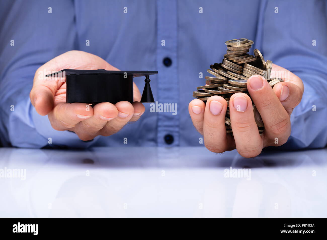 Close-up di una persona della mano che tiene la laurea Hat e monete su scrivania Foto Stock