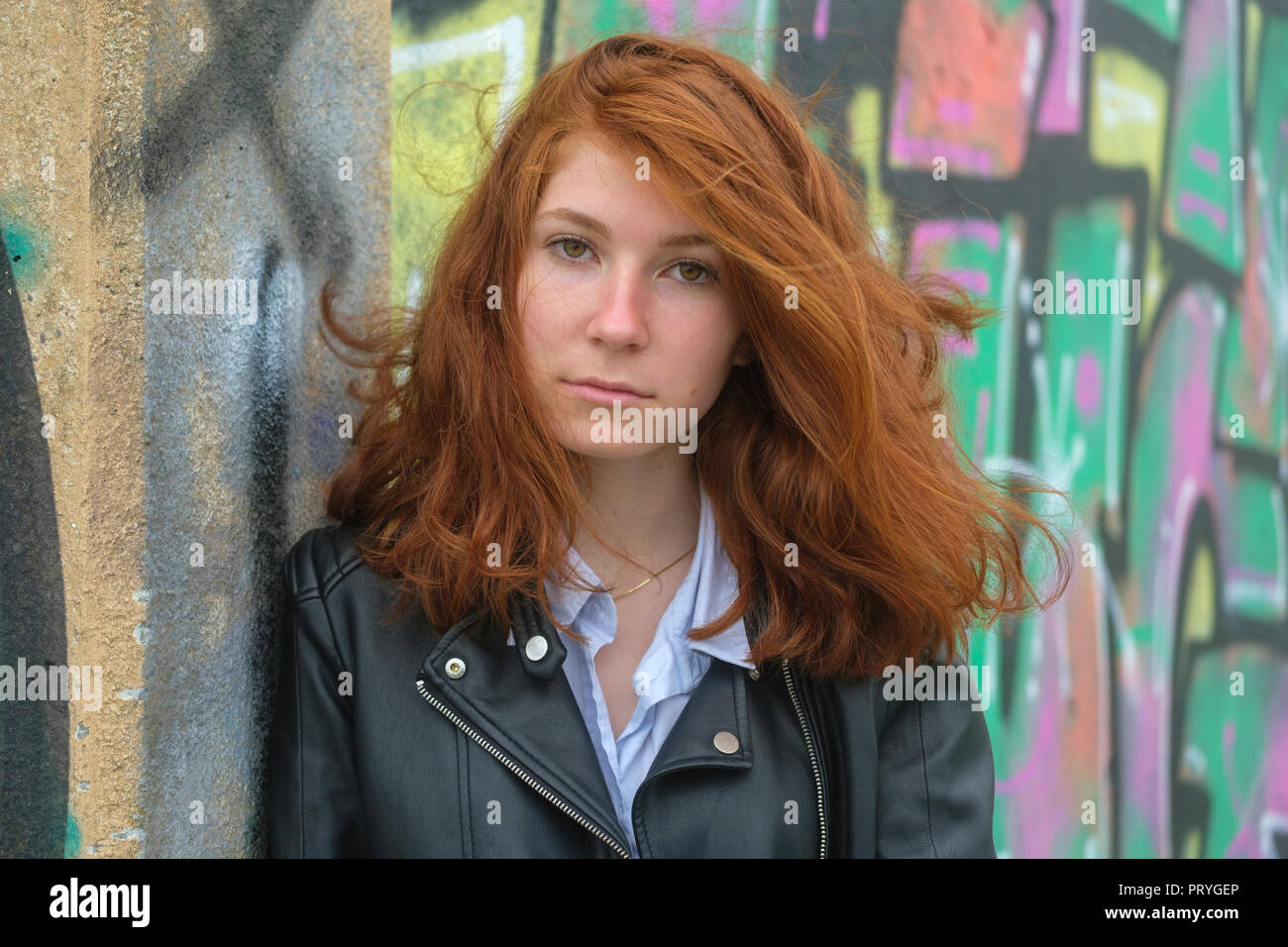 Ritratto, redheaded girl, giovane donna in giacca di pelle nella parte anteriore dei graffiti, a Finale Ligure e la Riviera di Ponente, Liguria Foto Stock