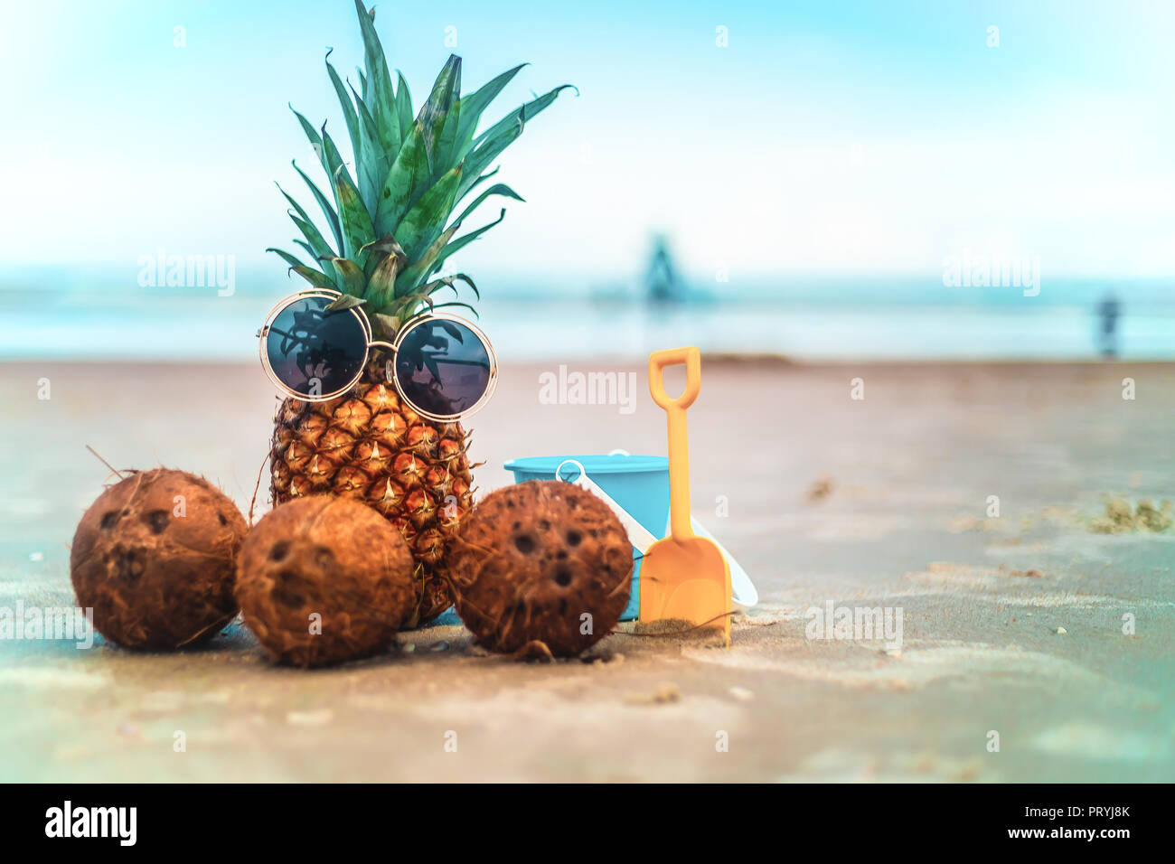 Carino ananas indossando occhiali da sole e noci di cocco rilassante sulla spiaggia Sunny Beach Foto Stock