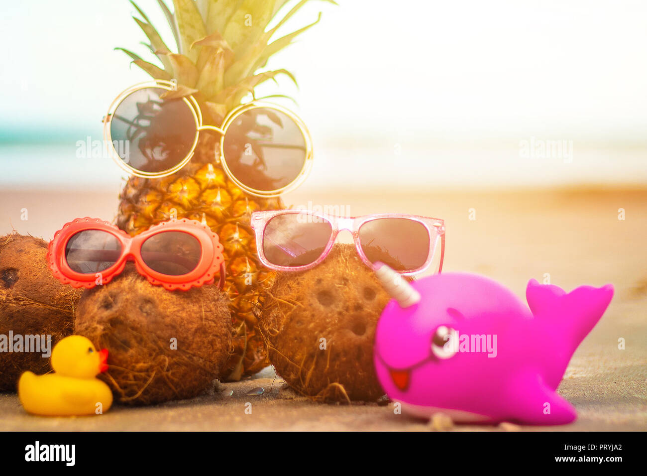 Adorabili e ananas e noci di cocco indossando occhiali da sole sulla soleggiata spiaggia tropicale Foto Stock