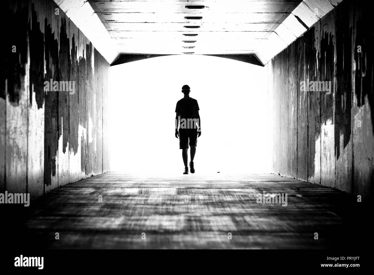 Silhouette di una persona in un tunnel, a camminare in avanti. Luce brilla in background. Foto Stock
