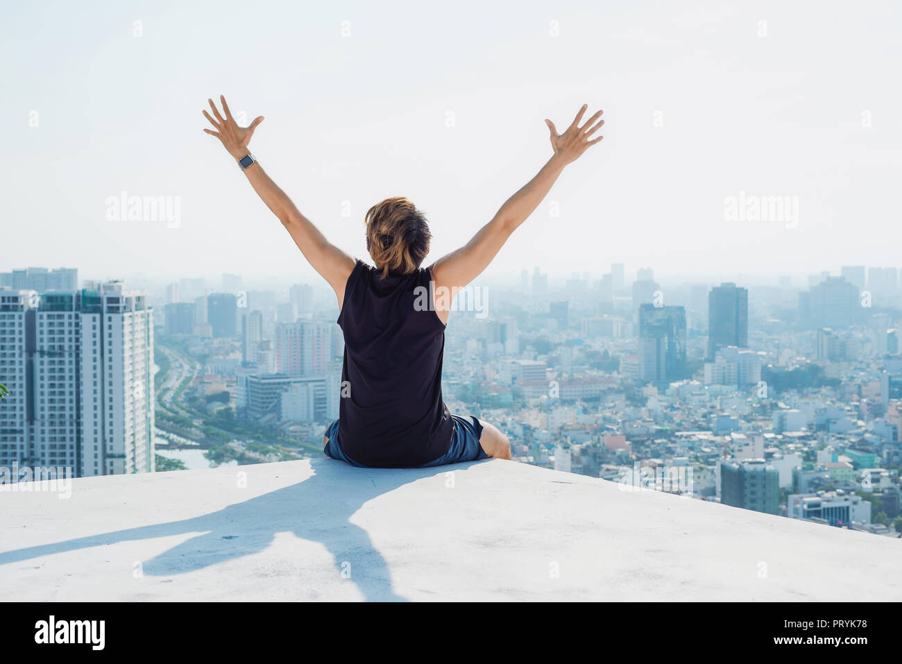 Uomo seduto sul tetto nero e mostra fino a mano con cielo blu di sfondo e sunshine,combattimenti uomo sul tetto Foto Stock