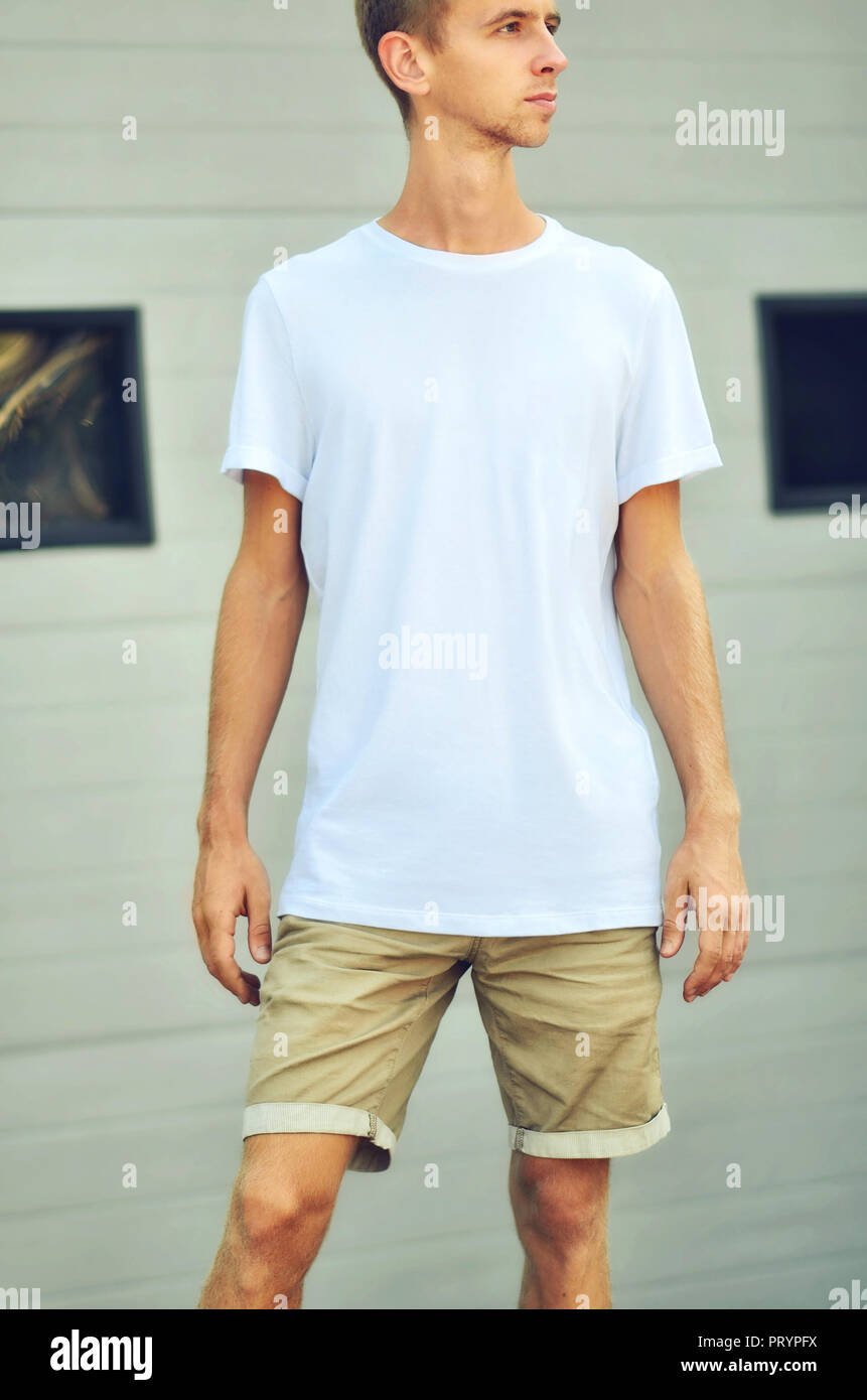 Urban mockup di vestiti. Elegante ragazzo in un fustellato T-shirt e  pantaloncini marrone stand vicino al bianco parete testurizzata con  finestre nere. Modello pronto per y Foto stock - Alamy