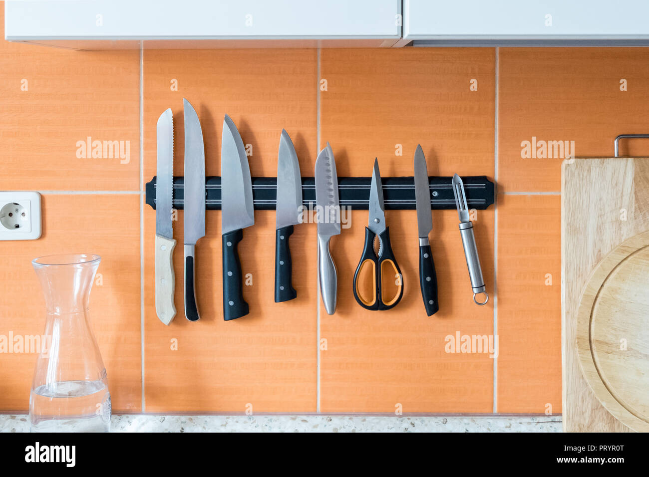 I coltelli sono appesi su un supporto magnete. Muro di cucina arancione. Un metodo di immagazzinare gli oggetti taglienti nella cucina Foto Stock