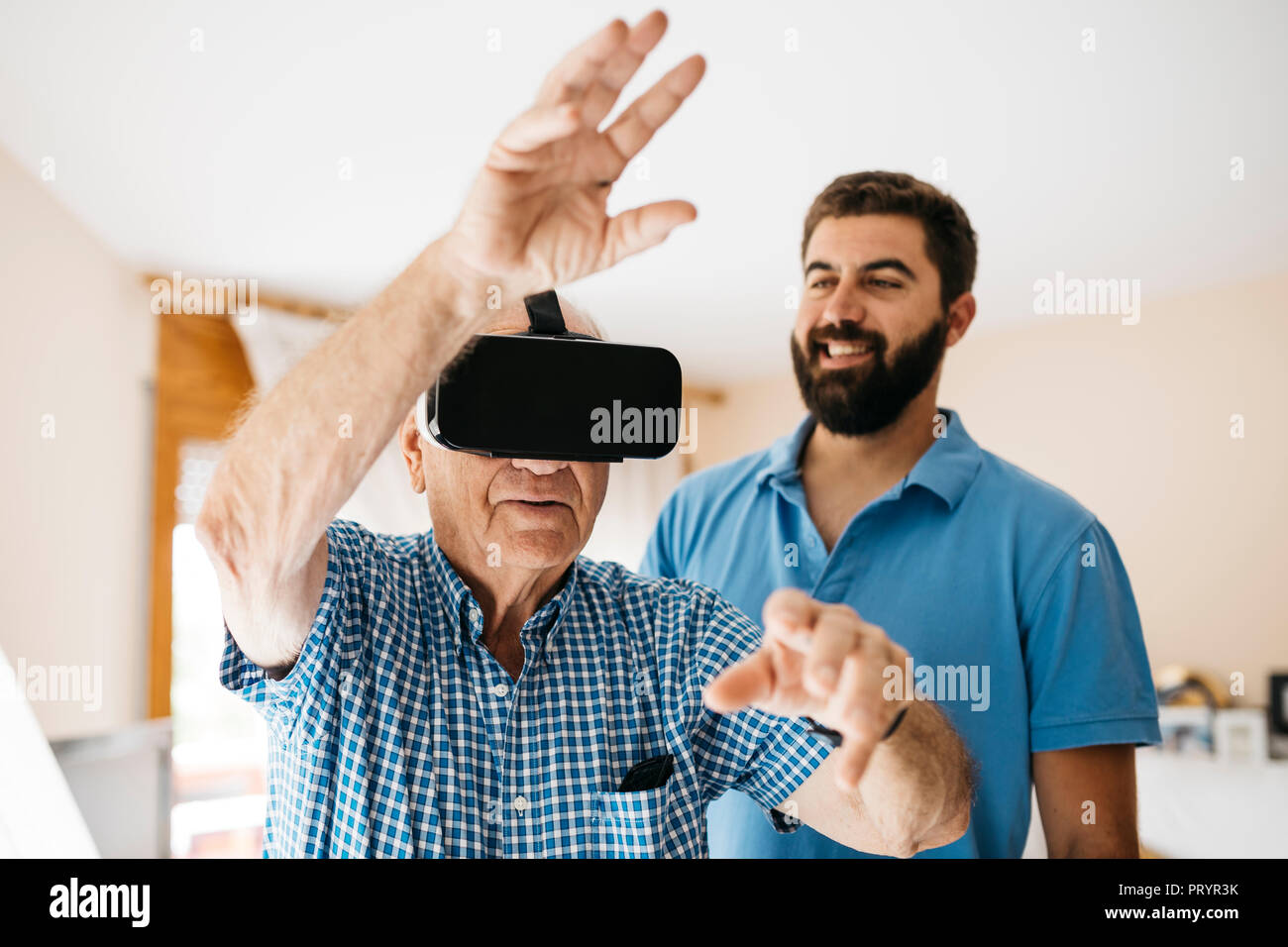 Senior Uomo con occhiali per realtà virtuale a casa mentre il suo nipote per adulti a guardare lui Foto Stock
