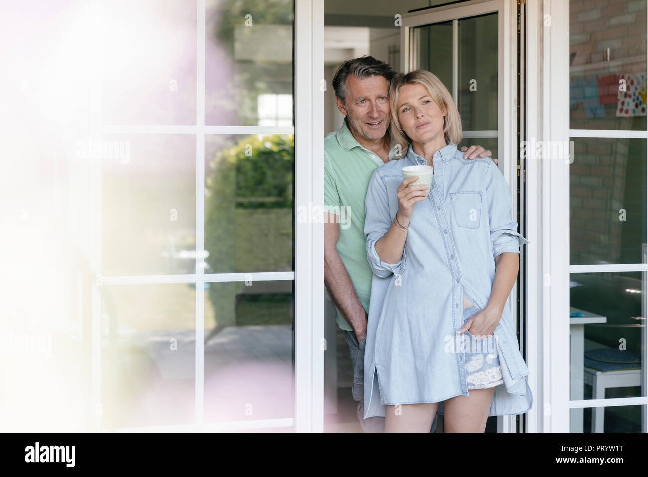 Sorridente Coppia matura in piedi alla finestra francese Foto Stock