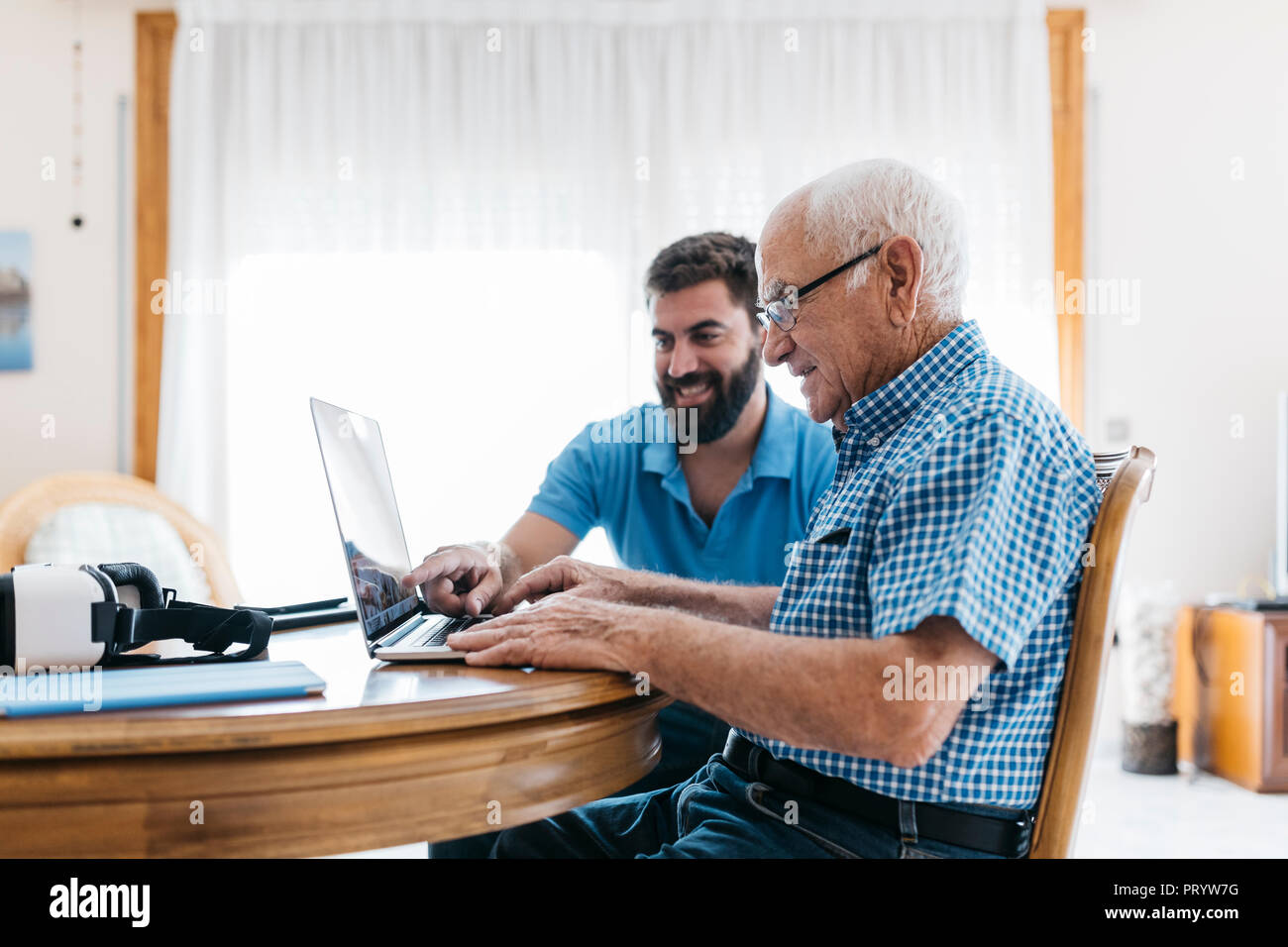 Nipote di adulti insegnamento a suo nonno per uso portatile Foto Stock