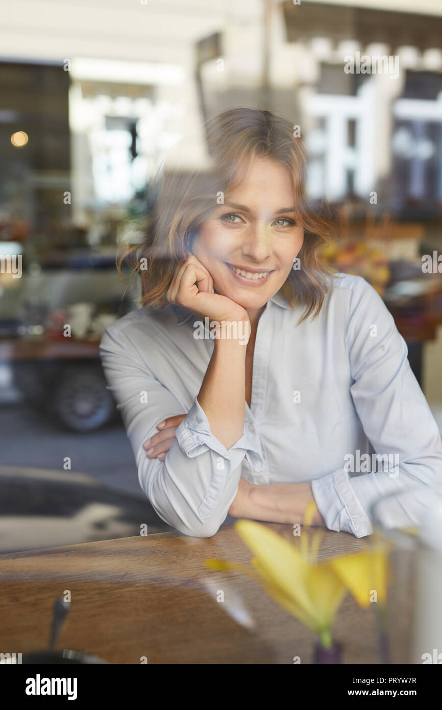 Ritratto di donna sorridente in un caffè guardando fuori della finestra Foto Stock