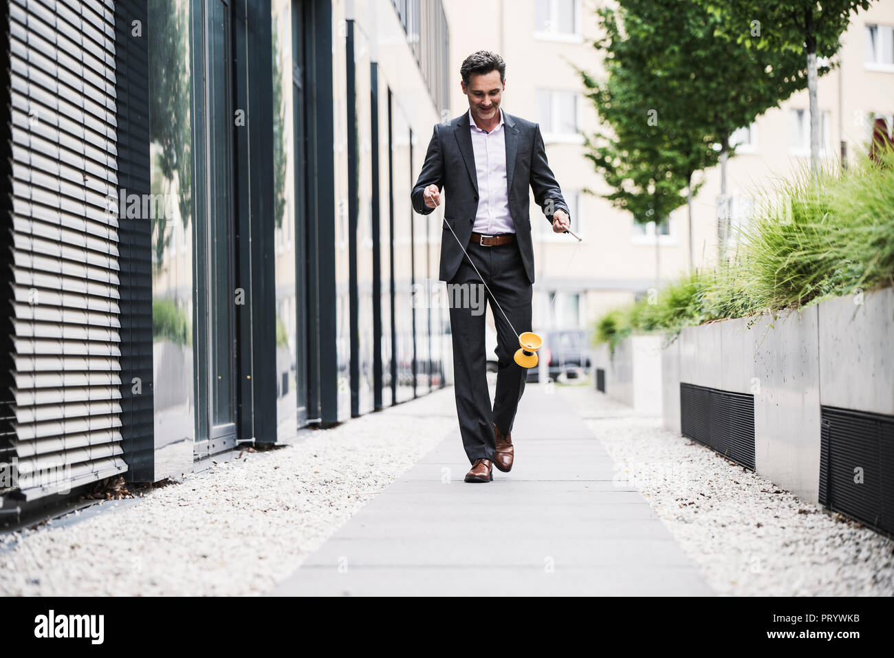 Imprenditore sorridente a piedi al di fuori ufficio edificio giocando con il diabolo Foto Stock