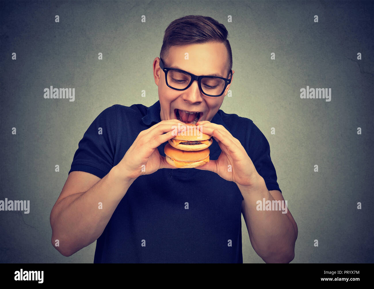 Uomo informale in bicchieri eccitato con doppio cheeseburger pur morendo di fame e di appetito per il fast food Foto Stock