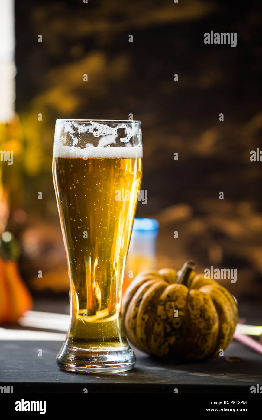 Bicchiere di birra dorata sulla scura, tavolo in legno, circondato da decorazioni di autunno Foto Stock