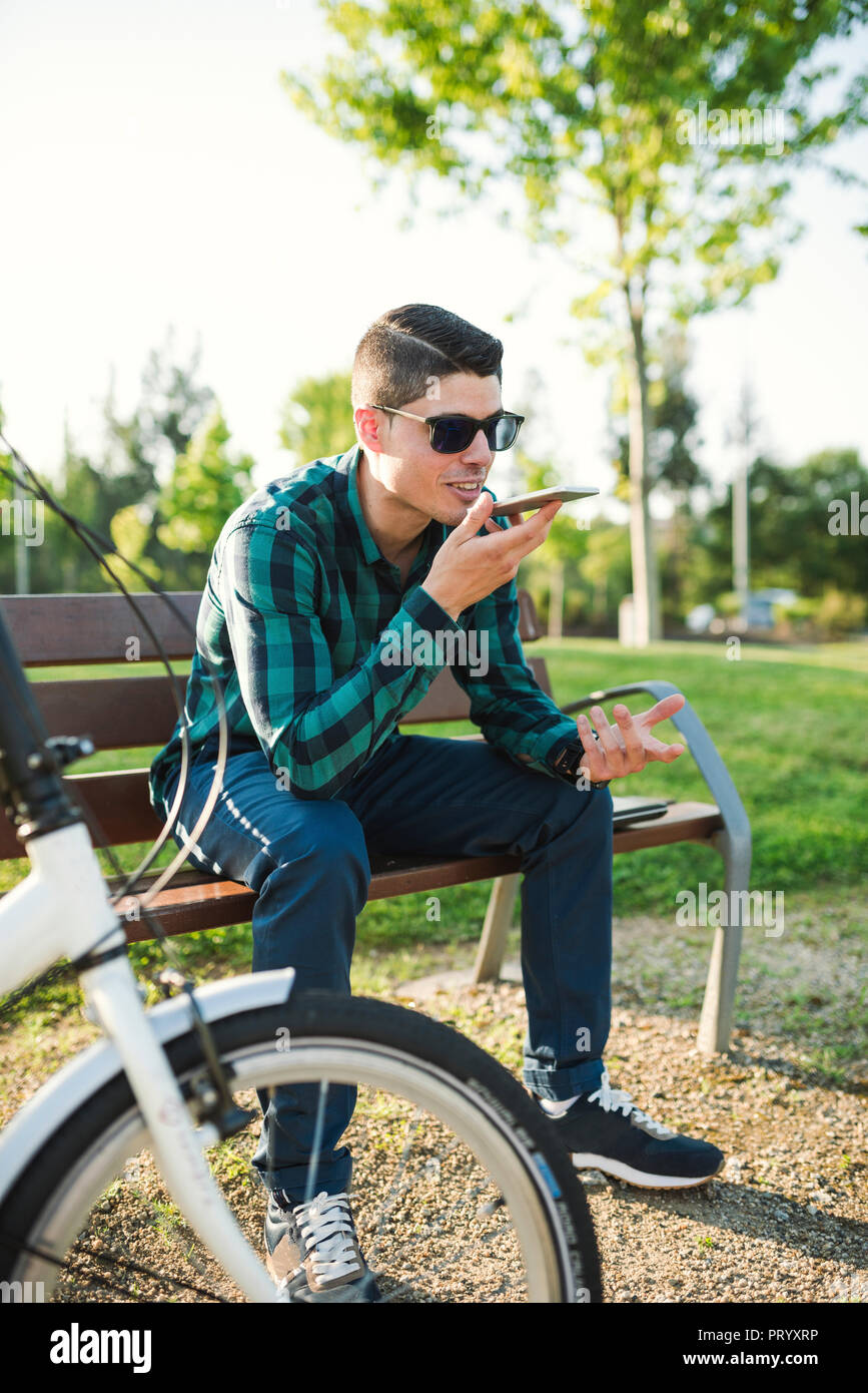 Giovane uomo inviando un messaggio di posta vocale in un parco Foto Stock