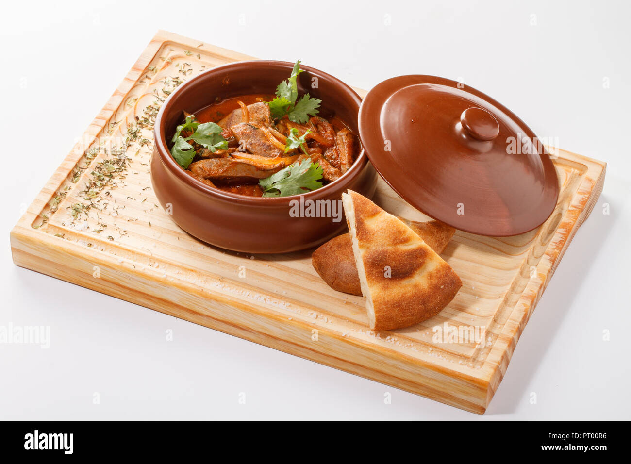 Tjvjik - fegato di agnello, cuore e polmoni stufati con cipolla e pomodoro -. Cucina armena tradizionale servita su tavola di legno su una pentola di argilla. Foto Stock