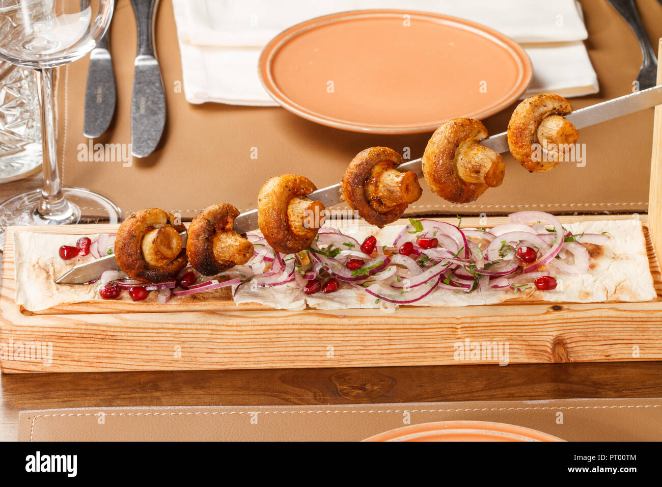 Grigliata di funghi Champignon su spiedini di metallo servita su una tavola di legno con pane e insalata di cipolla. Foto Stock