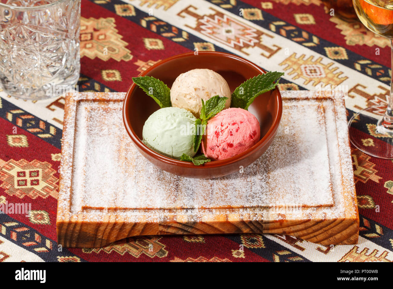 Gelato alla crema con le foglie di menta servito in una ciotola sulla parte superiore di una tavola di legno su un tradizionale tovaglia armena. 3 palline; lampone, pistacchio e caramello Foto Stock