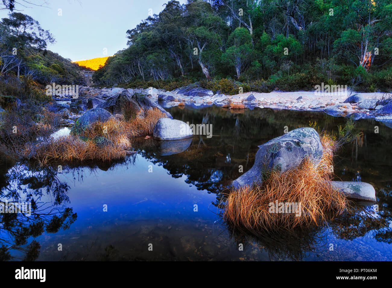 Specchio di calma superficie di acqua di fiume innevate nella stagione invernale sotto Guthega diga in alta montagna innevata di Australia tra neve-gum boschi a sunrise. Foto Stock