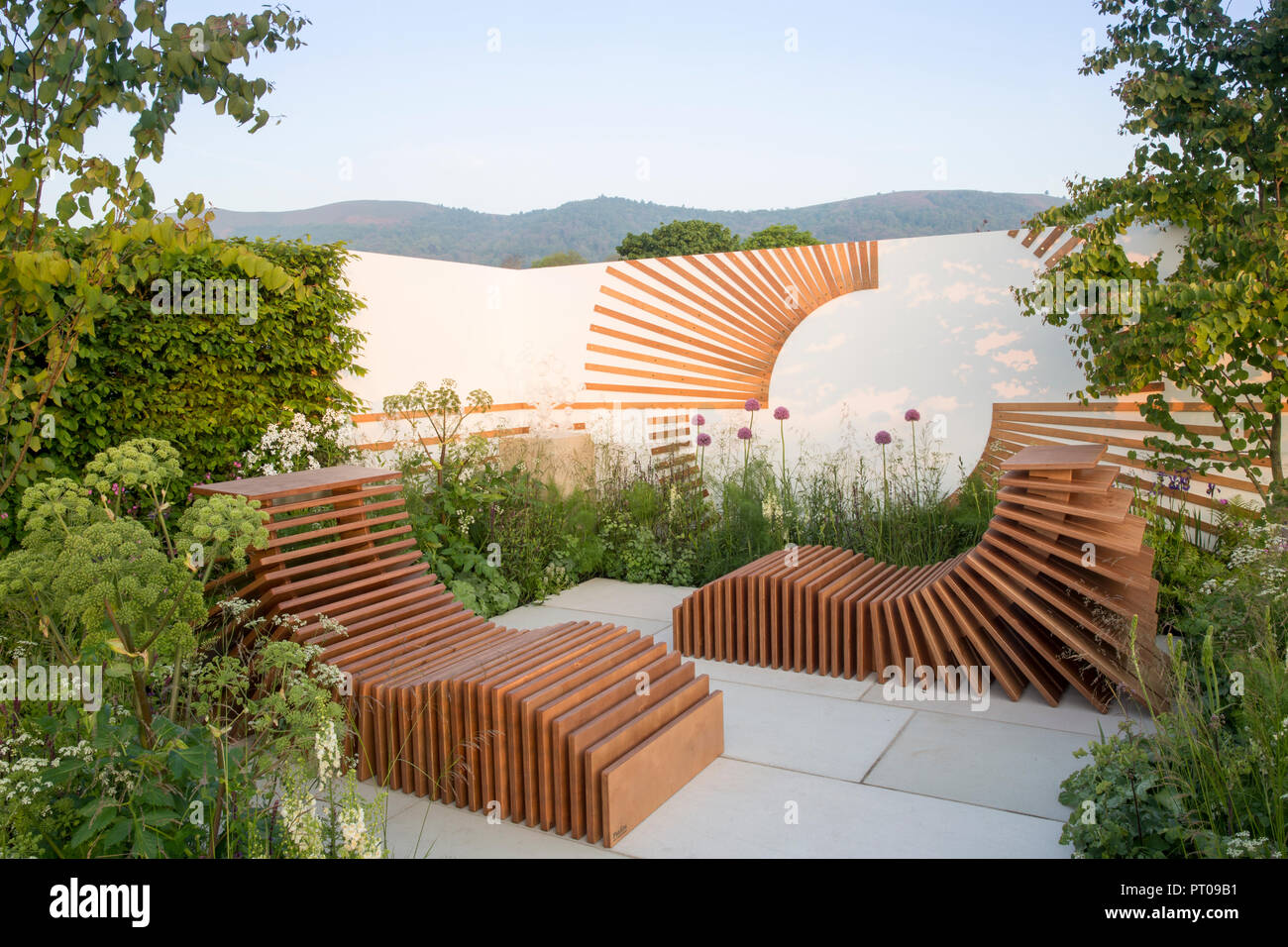 Piccolo cortile con giardino con patio in pietra, mobili da giardino in legno all'aperto, sedie reclinabili in corda di Allium e alberi UK Foto Stock