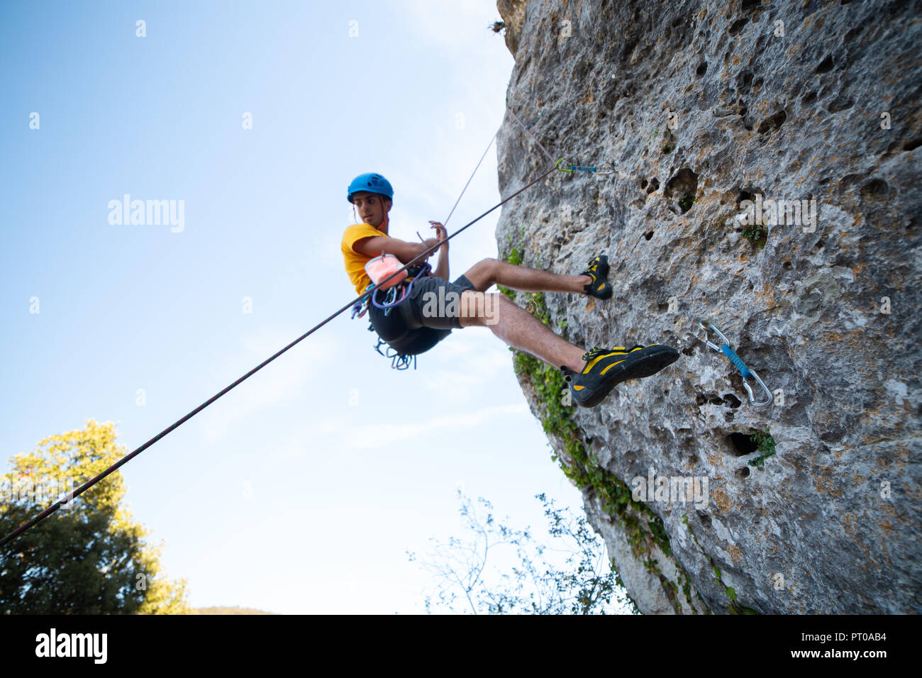 Da sotto tiro dei maschi di scalatore arrampicata in montagna sulla parete incredibile giornata di sole Foto Stock