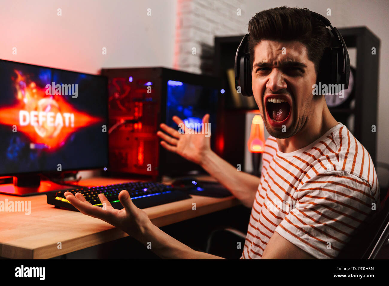 Vista laterale di Angry gamer per giocare con i videogiochi su computer e urlando mentre guardando la telecamera a casa Foto Stock