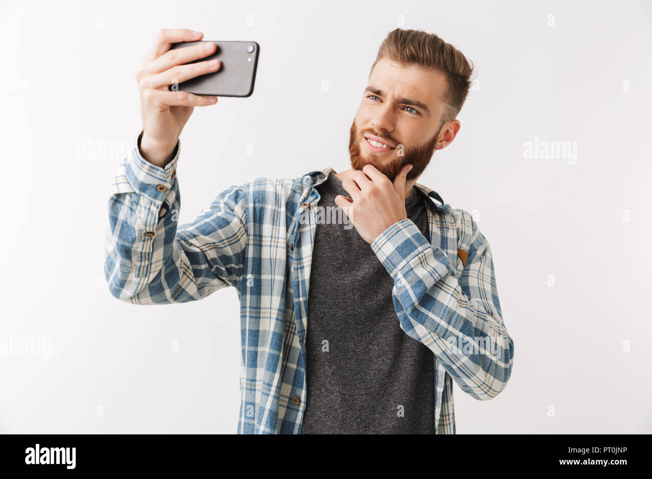 Ritratto di un allegro giovane uomo barbuto in piedi isolato su bianco, prendendo un selfie Foto Stock