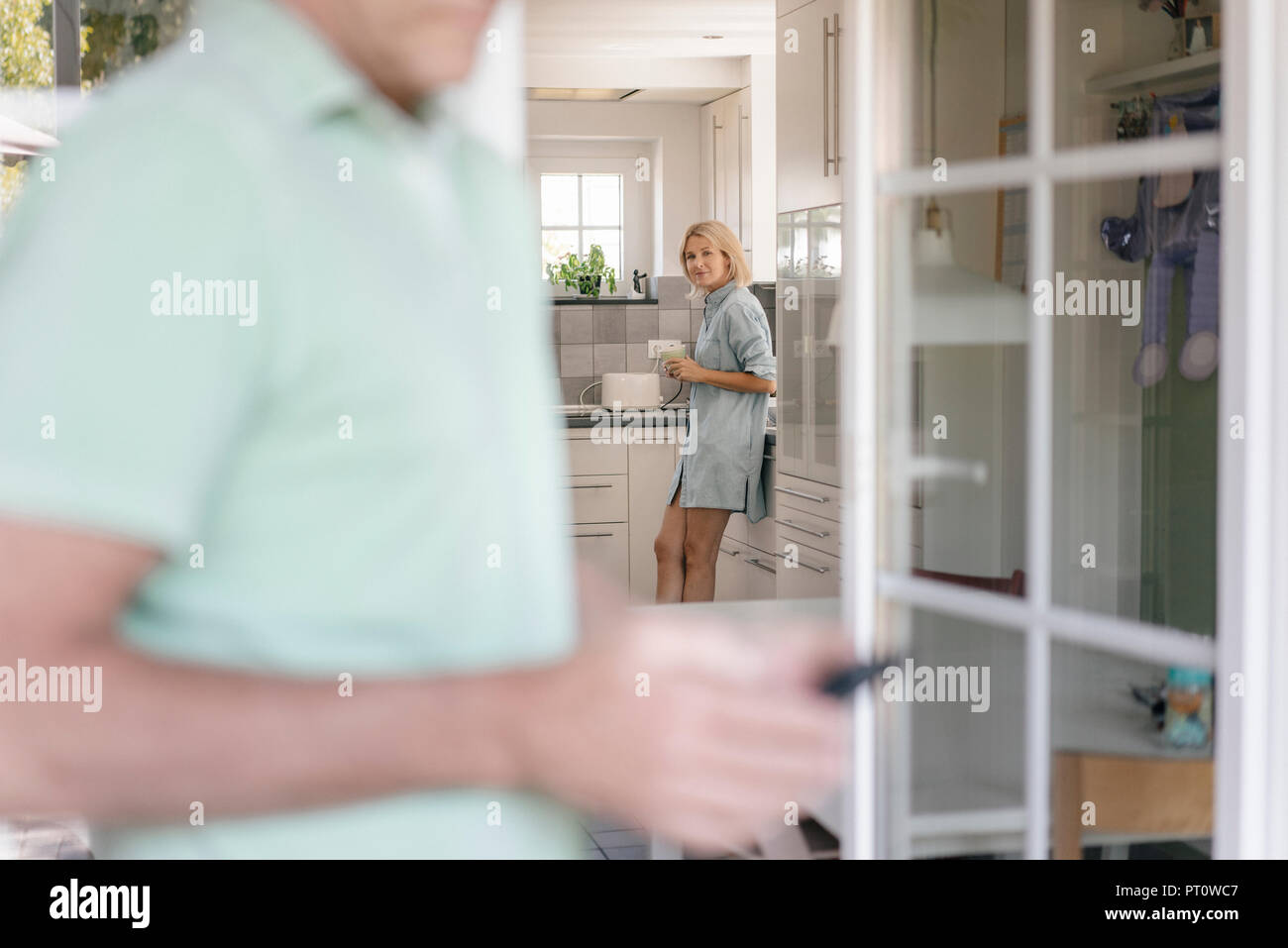 Donna matura in cucina a casa con uomo in primo piano Foto Stock