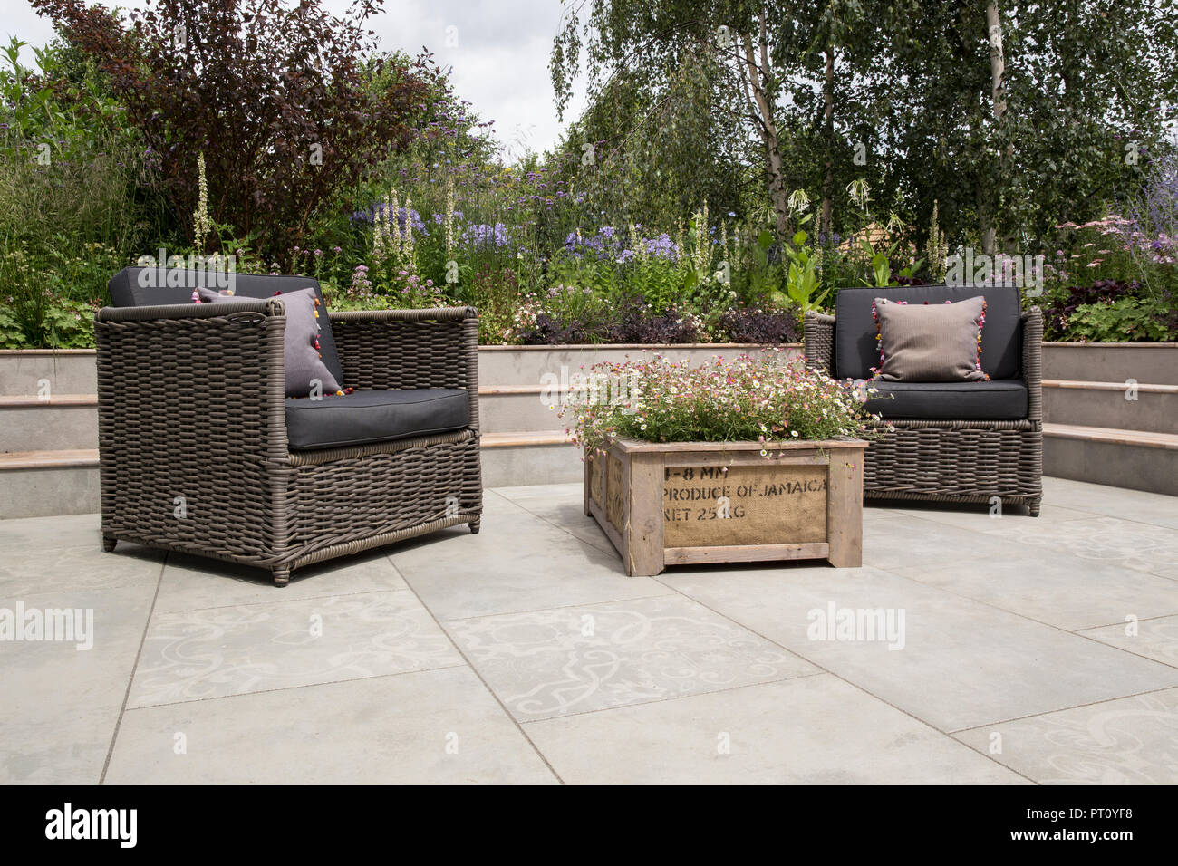 Moderno patio affondato giardino rialzato letto aiuole pavimento in pietra porcellana su area patio con legno crato pianter sedie da esterno mobili da giardino UK Foto Stock