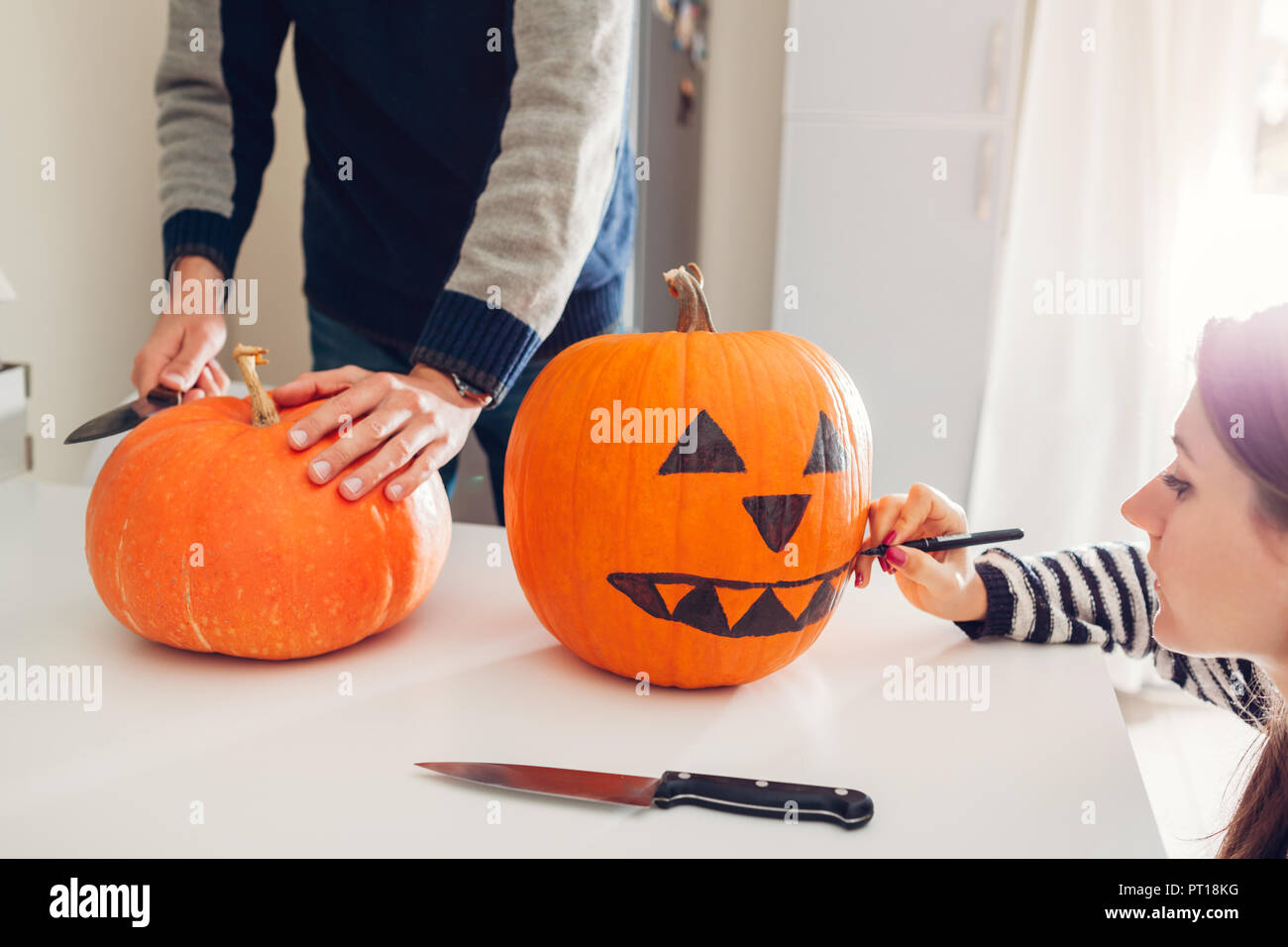 Coppia giovane rendendo jack-o-lantern per la festa di Halloween in cucina. Taglio e disegno di zucca. Decorazioni per le feste Foto Stock