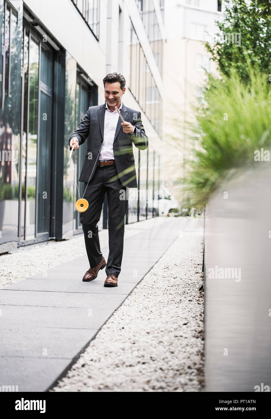 Imprenditore sorridente a piedi al di fuori ufficio edificio giocando con il diabolo Foto Stock