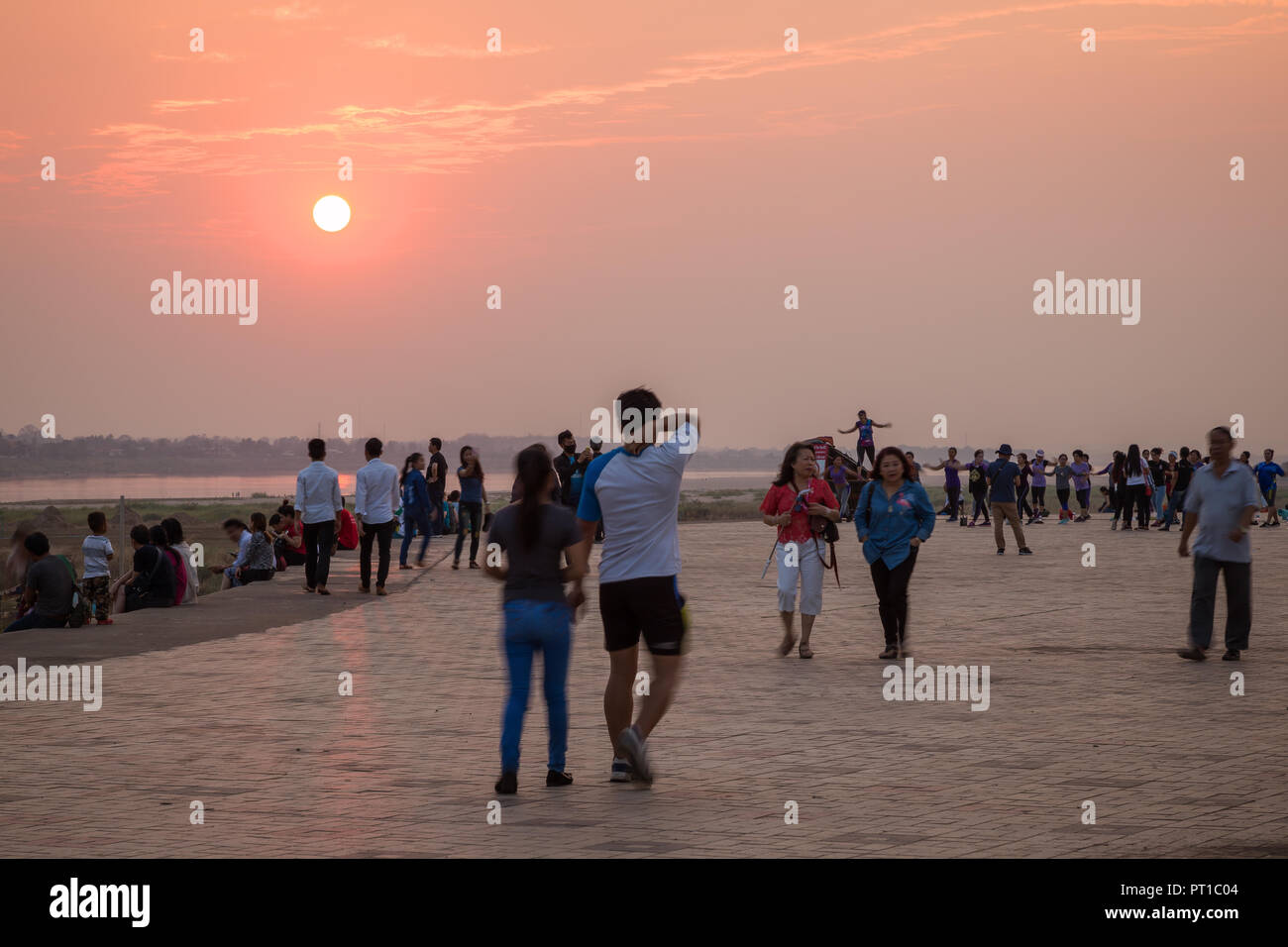 Turisti e gente locale seduta, rilassanti passeggiate ed esercitare presso la popolare Mekong Riverside Park di Vientiane, Laos, al tramonto. Foto Stock