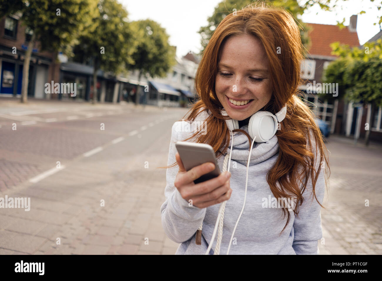 Redheaded donna usando le cuffie e lo smartphone nella città Foto Stock