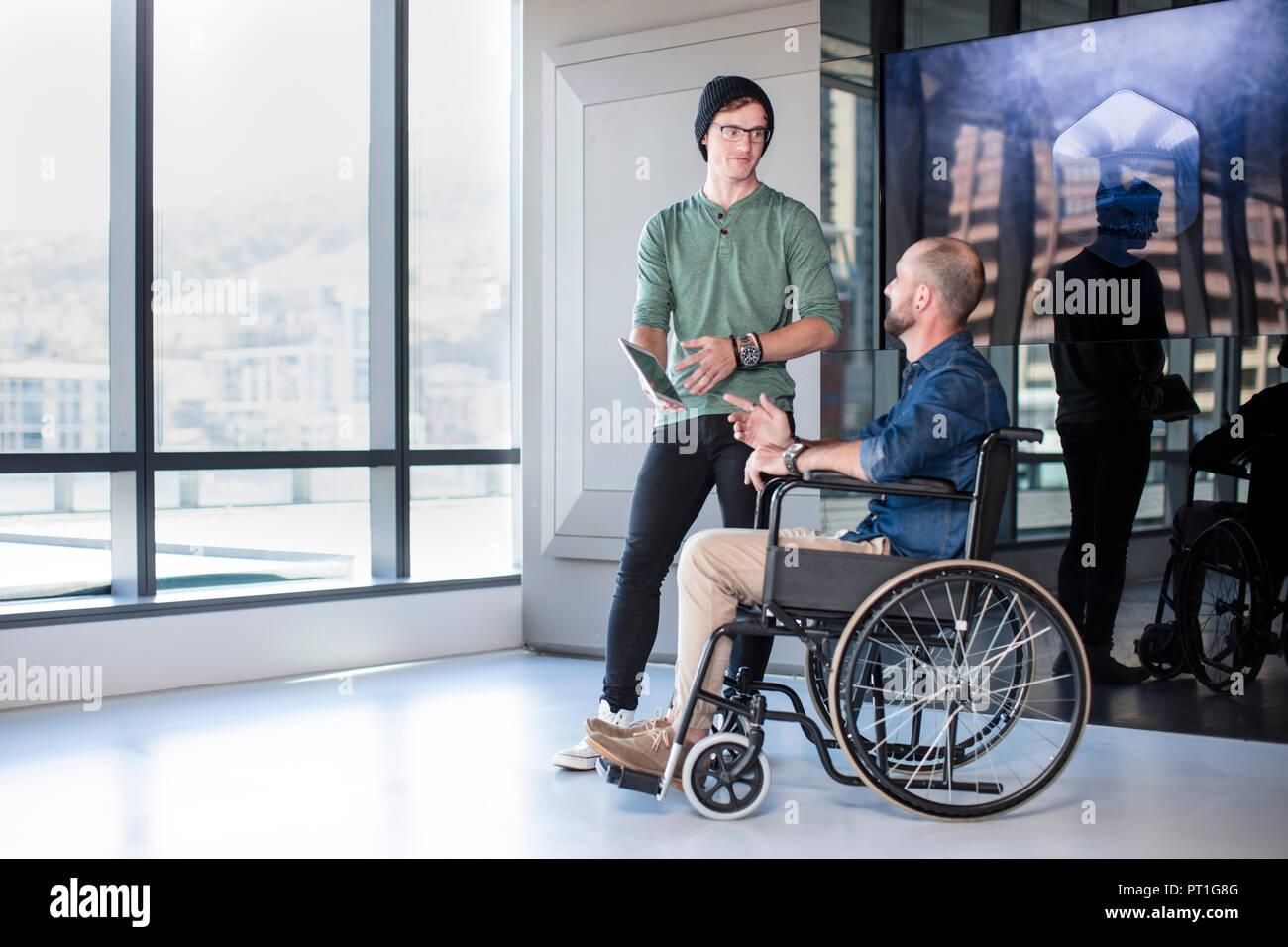 Uomo che parla al collega di portatori di handicap in carrozzina Foto Stock