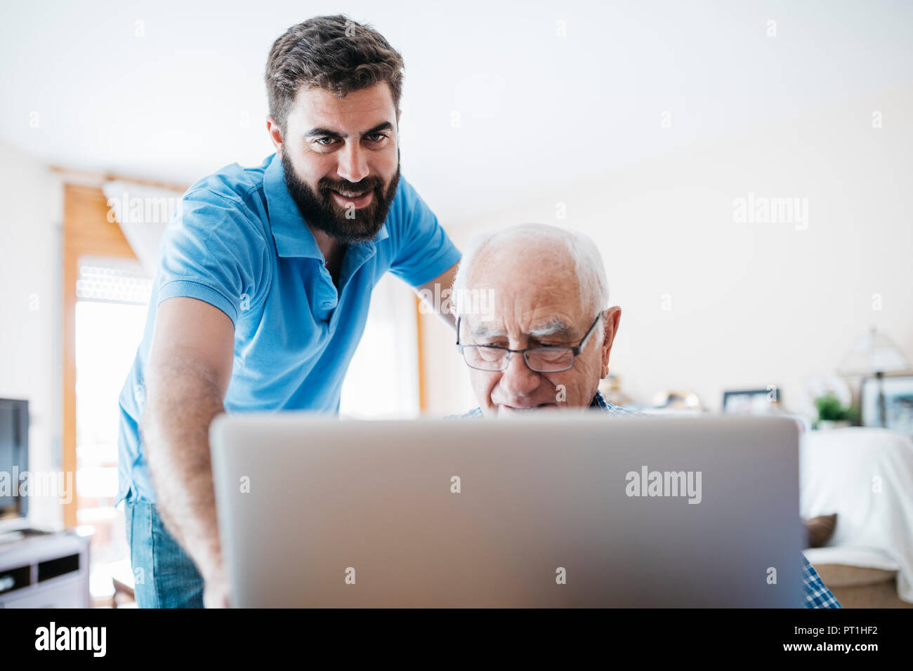 Nipote di adulti insegnamento a suo nonno per uso portatile Foto Stock