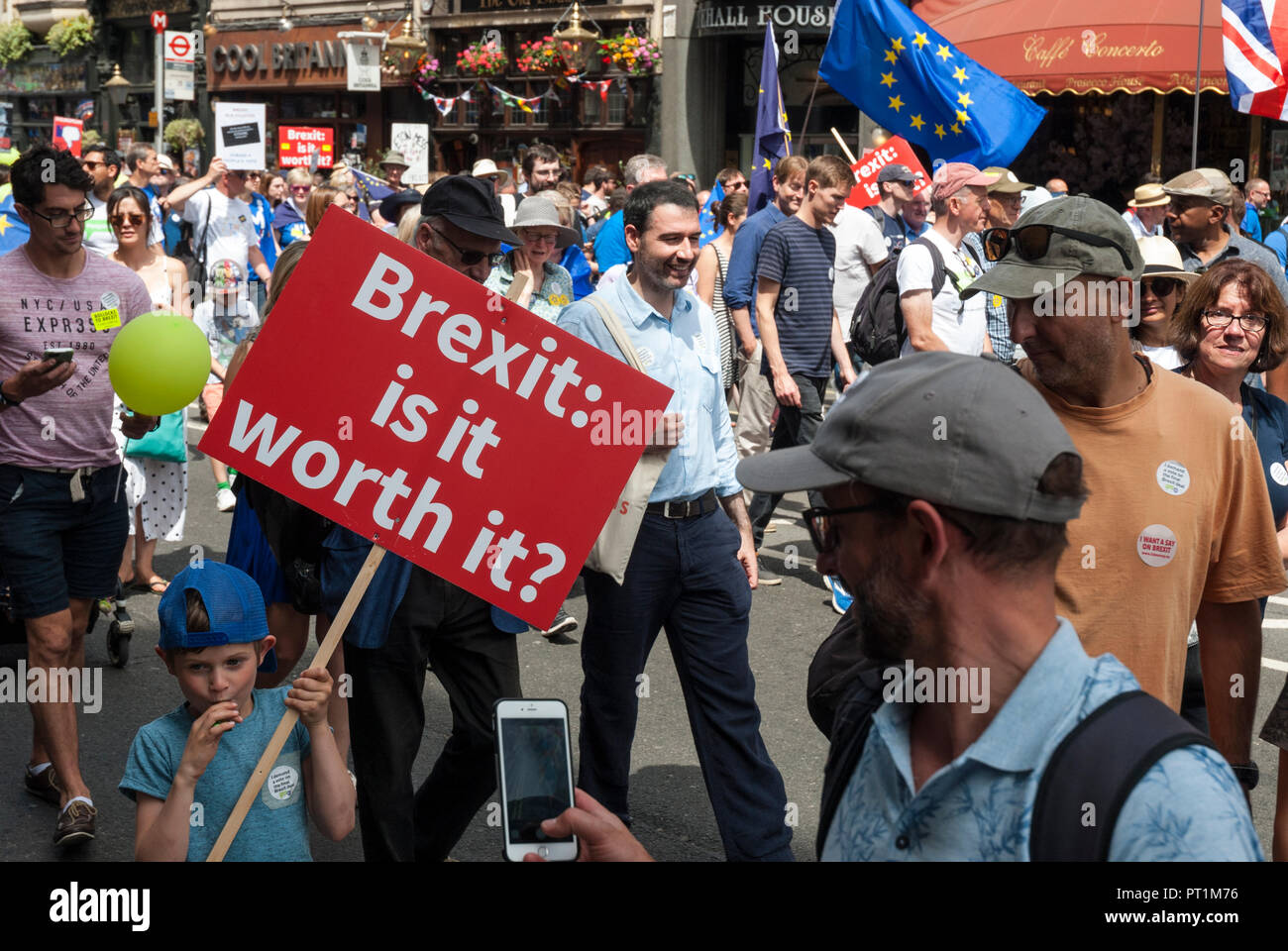 Ripresa a tutto campo della anti-brexit rally con un giovane ragazzo che trasportano rosso e poster whaite 'Brexit: ne vale la pena', dietro è blu bandiera UE con stelle d'oro. Foto Stock