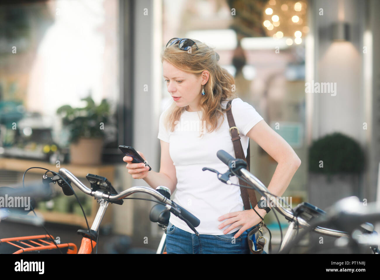 Germania, giovane donna con lo smartphone affittare una bici da città Foto Stock