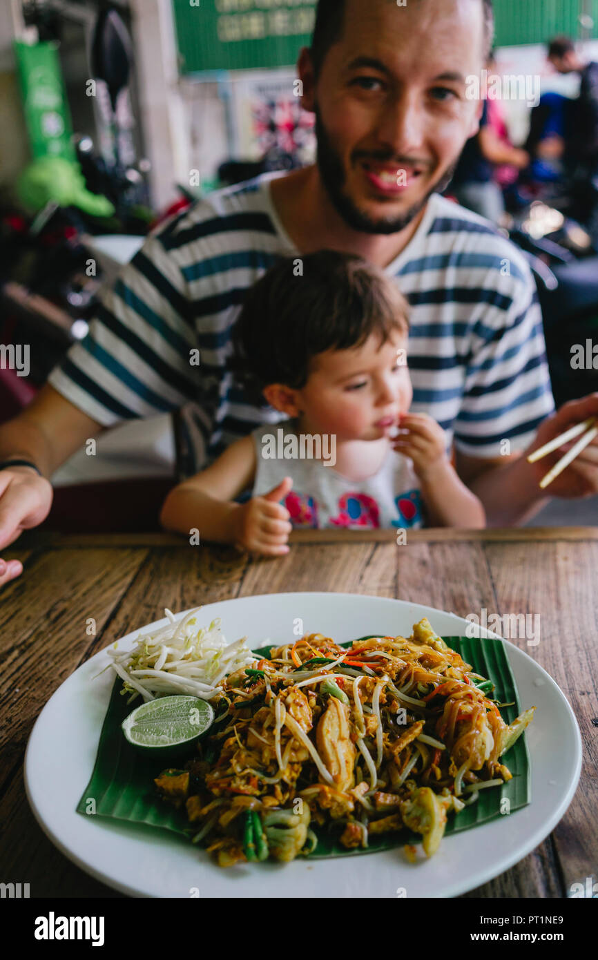 Thailandia, padre e figlia mangiare deliziosa pad thai piatto su una strada ristorante Foto Stock