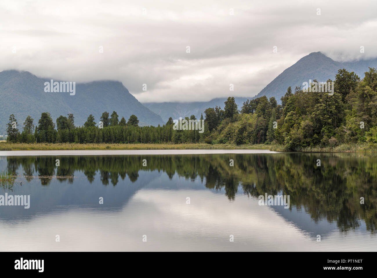 Il lago Matheson riflessioni sotto un cielo moody, villaggio Fox Glacier, West Coast, regione di South Island, in Nuova Zelanda, Foto Stock