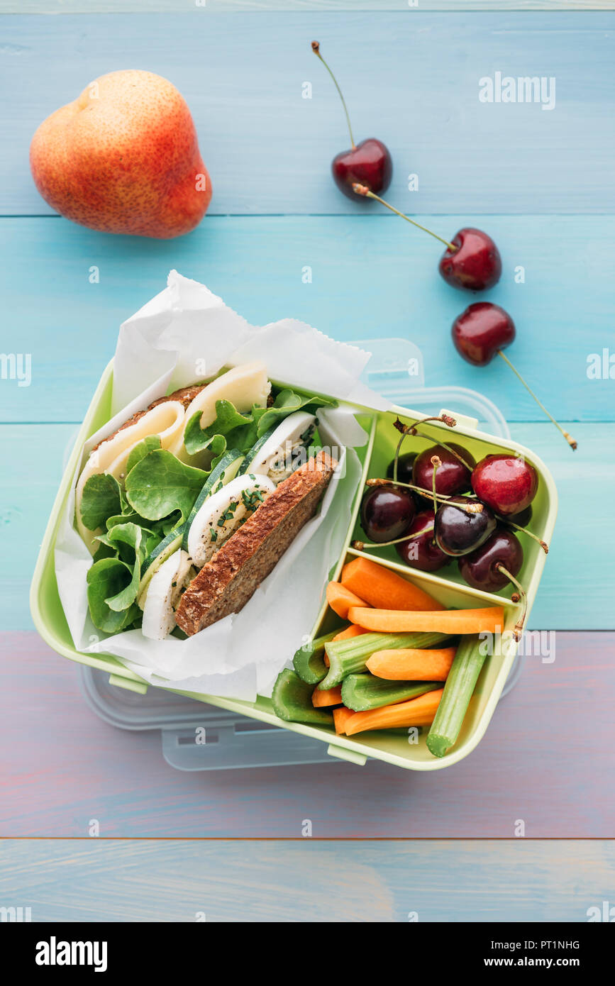 Scuola di sano cibo in una scatola di pranzo, sandwich vegetariano con formaggio, lattuga, cetriolo, uova e crescione, fette di carota e sedano, ciliegie e pera Foto Stock