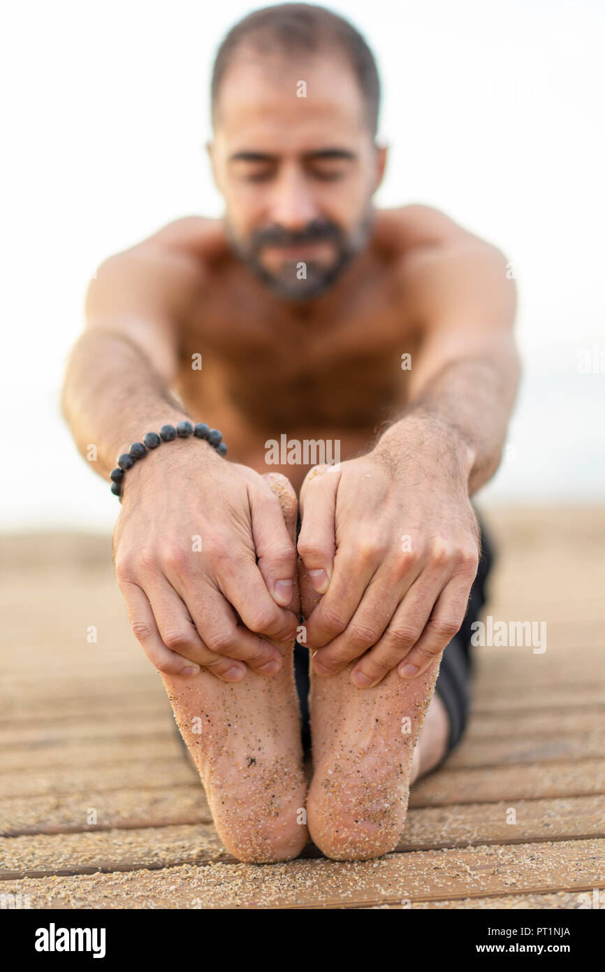 Spagna. L'uomo fare yoga sulla spiaggia la sera, stretching gambe, mani e le suole dei piedi Foto Stock