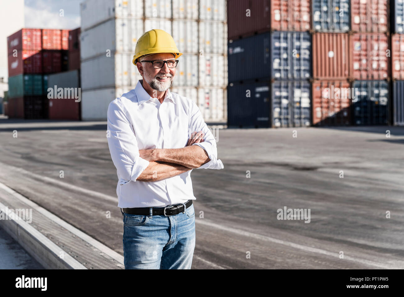 Imprenditore al porto di carico, indossando il casco di sicurezza, con le braccia incrociate Foto Stock