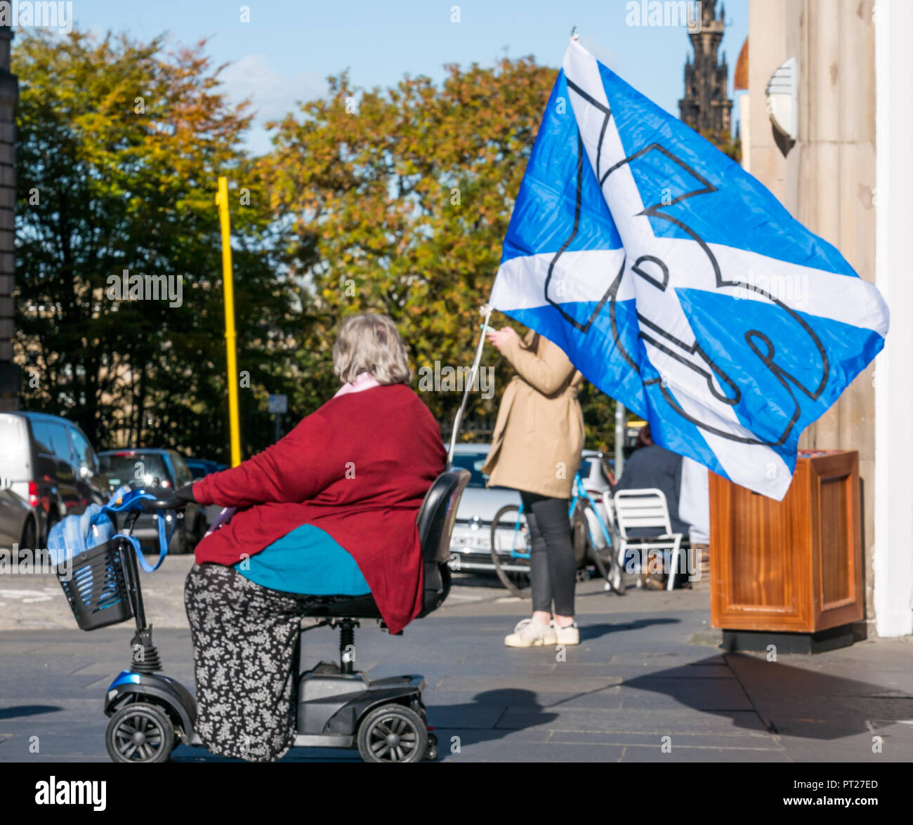 Holyrood, Edimburgo, Scozia, Regno Unito, 6 ottobre 2018. Tutti sotto uno striscione (AUOB) Scottish marzo Rally e per l'indipendenza, con tifosi percorrendo a piedi il Royal Mile a Holyrood Park per un rally. AOUB è un pro-indipendenza campagna per il cui obiettivo principale è quello di marzo ad intervalli regolari fino a quando non raggiunge la Scozia indipendenza. Un disabile donna più anziana in una mobilità scooter con un scozzese St Andrews Cross si intraversa bandiera Foto Stock