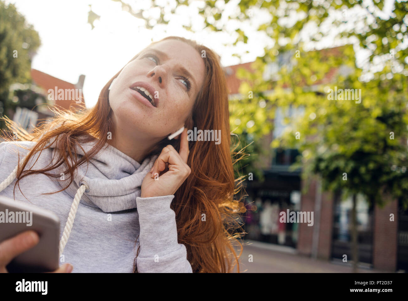 Redheaded donna utilizzando gli auricolari dello smartphone e Foto Stock