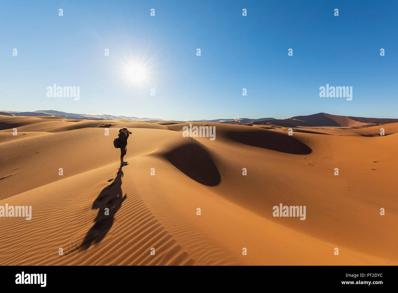 In Africa, la Namibia, il deserto del Namib Naukluft, Parco Nazionale, photograper femmina sulla duna di sabbia contro il sole Foto Stock